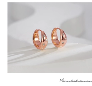 Macro shot of rose gold hoop earrings with micro-inlaid zirconium on white marble base
