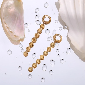 Detail of gold-plated snowflake chain earrings on a mirror background with sea shells