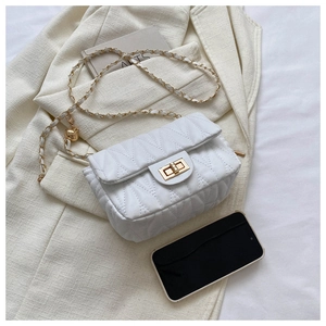 White quilted crossbody bag with gold chain strap styled on a beige suit and art books