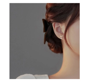 Close-up of a gold bow earring with a sparkling white zircon drop on a female ear