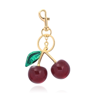 Detail of red cherry bag charm with green leaf and golden glitter resin texture
