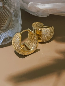 Macro shot of gold plated hoop earrings with micro-paved white zircons on a warm surface