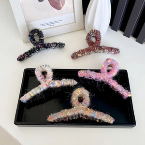 Detailed view of wave-shaped large hair claws in five soft knitted yarn colors