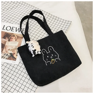 Detail of black corduroy tote bag with rabbit embroidery and cow plush keychain charm