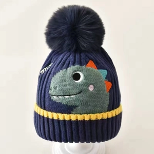 Dark blue knitted baby hat featuring green dinosaur embroidery and a large pom-pom