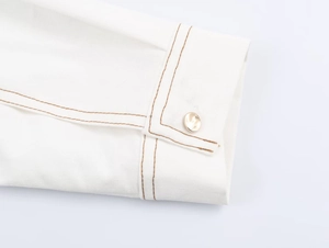 Détail du poignet de chemise blanche avec surpiqûres marron contrastées et bouton doré