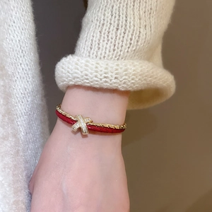 Détail du bracelet en cuir tressé rouge et chaîne dorée avec élément croisé en cristaux