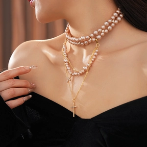 Close-up of double-layer necklace with pink pearls and golden cross pendants on model