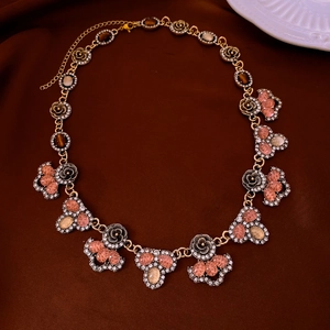 Macro shot of vintage gold flower necklace with pink gems on dark velvet background