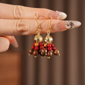 Close-up of Bohemian gold hook earrings with red beads and wood grain tassels