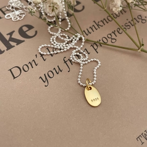 Elegant S925 sterling silver LOVE necklace with two-tone oval pendant on beige paper