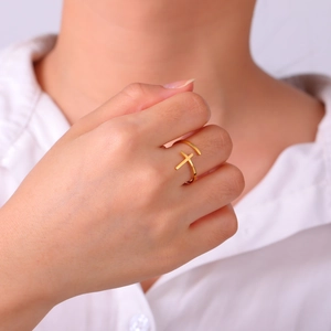 Detailed view of an adjustable gold cross ring worn on a model's finger
