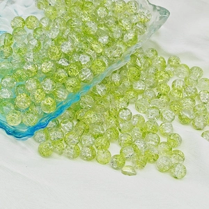 Macro shot of 6mm and 8mm green crackle glass beads scattered on white textured fabric