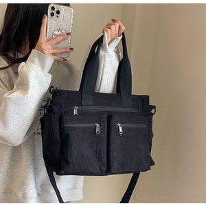 Detailed view of black corduroy tote bag featuring three front zippers and adjustable strap