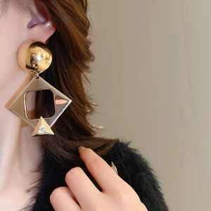 Close-up of geometric gold drop earrings with crystals worn by a model