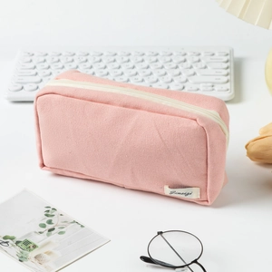 Close-up of pink canvas pencil case with zipper and woven label on a white desk