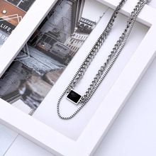 Gros plan d'un collier double épaisseur avec pendentif rectangulaire et chaîne gourmette