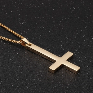 Detailed close-up of a gold-plated titanium cross pendant on a black textured background