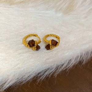 Detail of gold-plated twisted hoop earrings with brown square zircon stone on soft fur