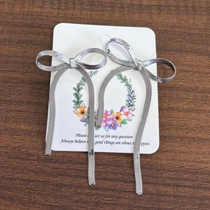 Detailed view of silver bow-shaped long tassel earrings with snake chain on wood surface