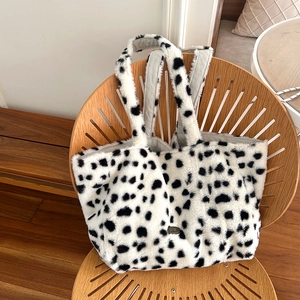 Close-up of plush cow print tote bag with soft faux fur texture on a wooden chair