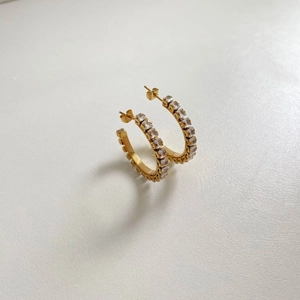 Detail of gold C-shaped earrings with clear zircon stones on a white background