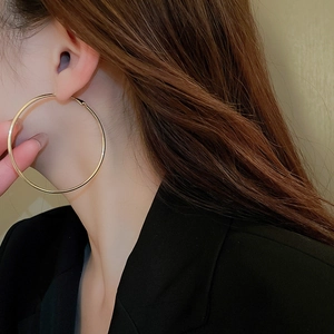 Close-up of a model wearing large polished gold hoop earrings with a minimalist design