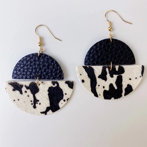 Détail de boucles d'oreilles imprimé vache en cuir noir et crochets dorés brillants