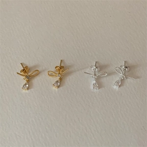 Detail of silver and gold bow earrings with pear-shaped drops and small cubic zirconia stones