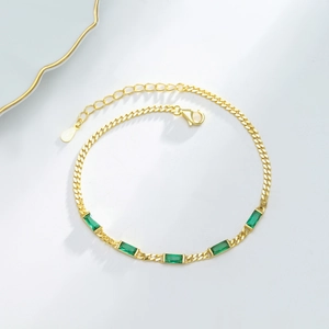 Close-up of gold chain bracelet featuring five green rectangular gemstones with clasp
