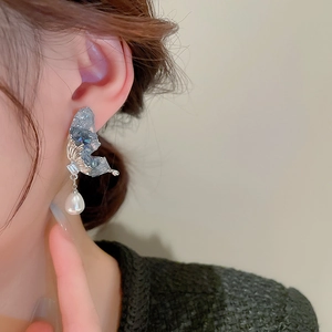 Close-up of elegant butterfly earrings with blue crystals and white pearl drops on model