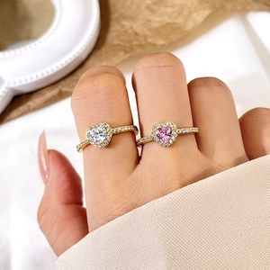 Detailed view of heart-shaped gold rings with pink and white stones worn on fingers