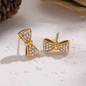 Boucles d'oreilles nœud dorées avec cristaux sur une surface blanche texturée