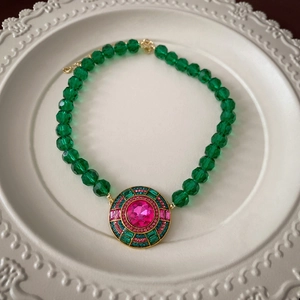 Detail of vintage palace style necklace with pink center stone and green faceted beads