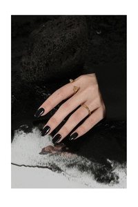 Detailed close-up of golden knot ring set on hand with black polish and volcanic rock background