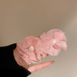Close-up of pink tulle flower earrings with pearl centers held by hand on warm background