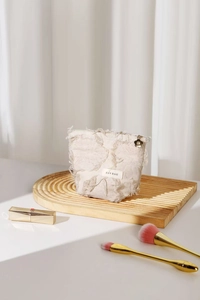 Close-up of cream linen cosmetic bag with frayed tassel fringe and golden flower zipper pull