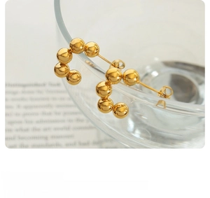 Detail of gold beaded C-shaped hoop earrings placed on a glass bowl with text background