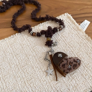 Détail macro du pendentif cœur en peluche léopard avec finitions en cuir et pompon