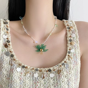 Dettaglio collana di perline con ciondolo a palma verde indossata sul collo