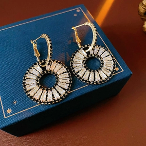 Macro shot of gold earrings with black circles and white zircon stones on jewelry box