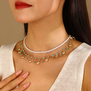 Détail du collier double couche en perles et chaîne dorée avec strass bleus et pendentifs cœur