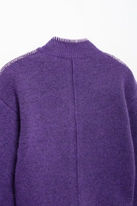 Dettaglio cardigan in maglia viola con cuciture bianche a contrasto su spalla e colletto