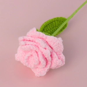 Close-up detail of a handmade pink crochet rose with green leaf on a soft pink background