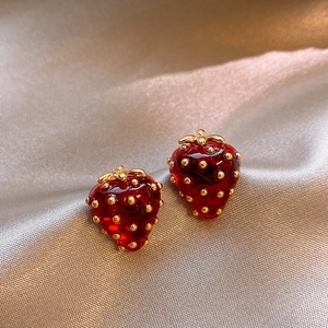 Elegantes pendientes de fresa en rojo y oro sobre un fondo de seda de color champán