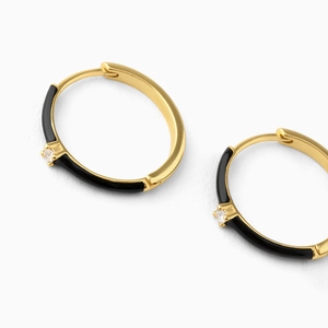 Close-up of gold-plated hoop earrings with black enamel inlay and sparkling zircon stone