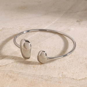 Gros plan d'un bracelet ouvert style métal liquide argenté sur fond de pierre naturelle