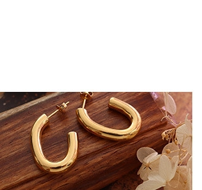 Macro shot of U-shaped gold-plated polished earrings on a wooden background with dried flowers