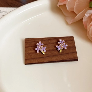 Dettaglio di orecchini a lobo a fiori viola in smalto con foglie dorate su legno