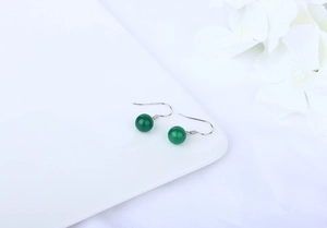 Close-up of elegant green agate ball earrings with polished silver hooks on a white petal